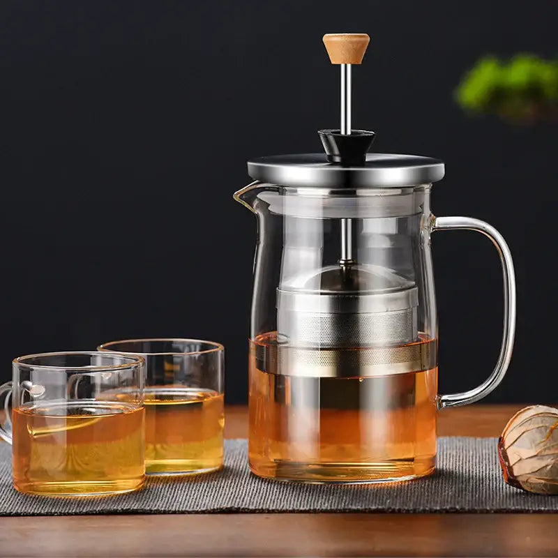 Decorbites glass tea pot featuring a clear glass body, stainless steel plunger, wooden handle, filled with amber tea