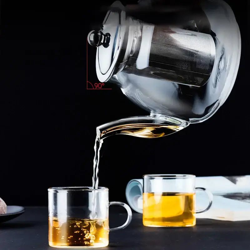 DecorBites glass tea pot with stainless steel filter and black knob pouring amber tea into matching glass cups