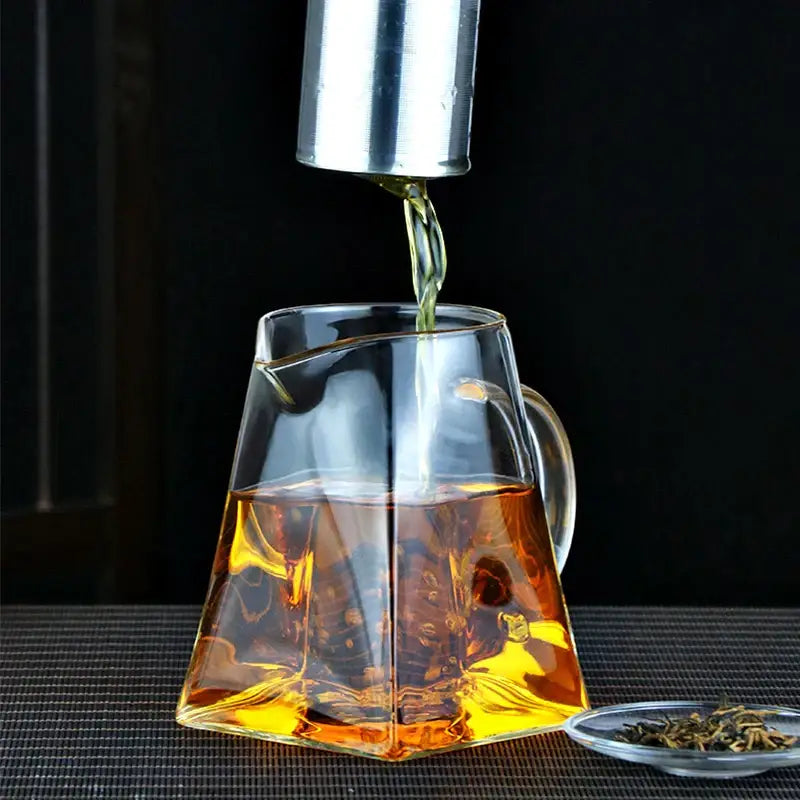 DecorBites glass tea pot with geometric design and stainless steel infuser filled with amber tea in clear glass