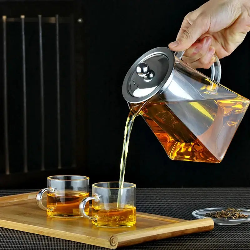 DecorBites glass tea pot with stainless steel infuser pouring amber tea into two clear glass cups