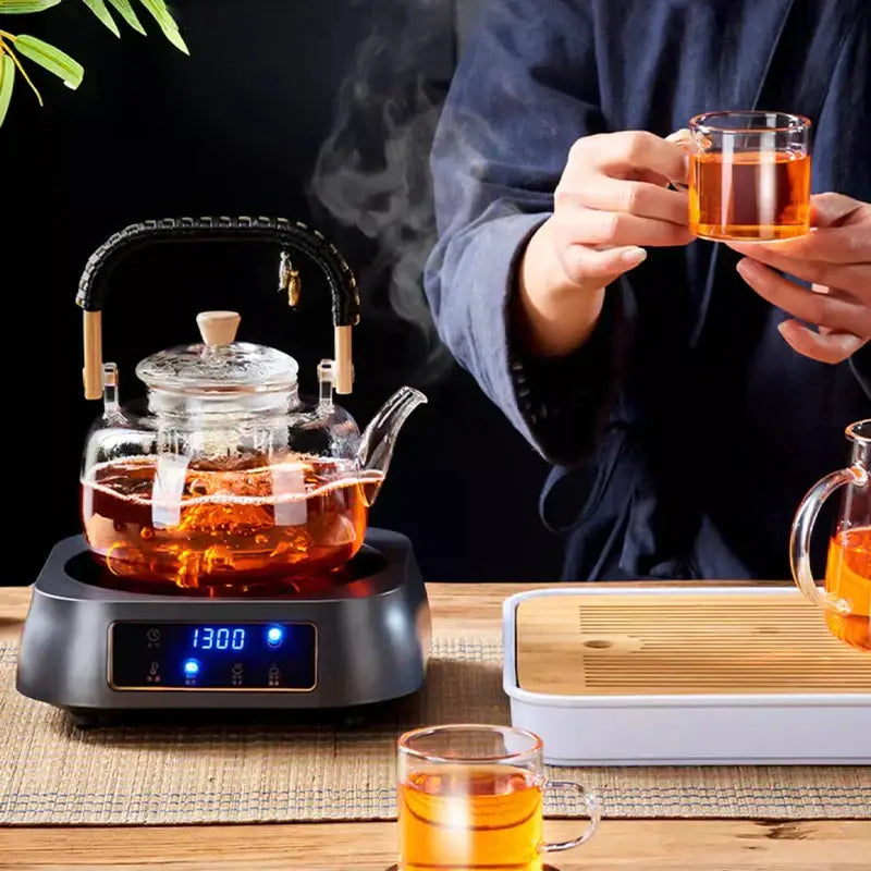 Clear glass DecorBites glass tea pot with black and wooden weave handle on electric heating base displaying 1300