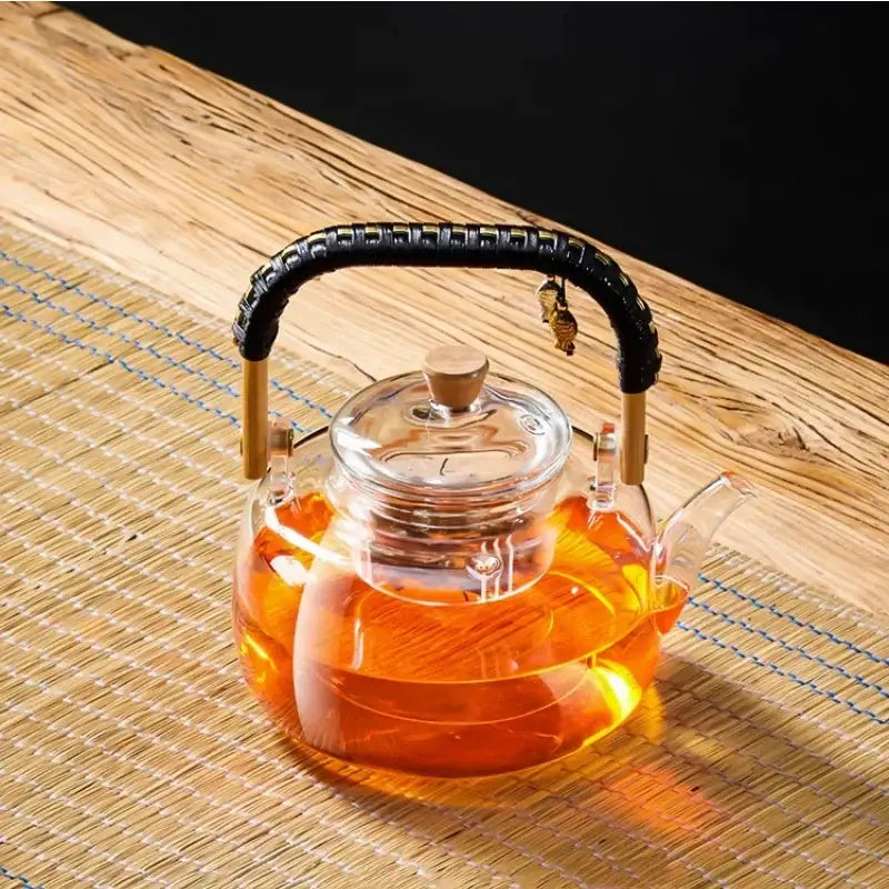 Clear glass decorbites glass tea pot with black weave handle wooden accents and amber tea inside