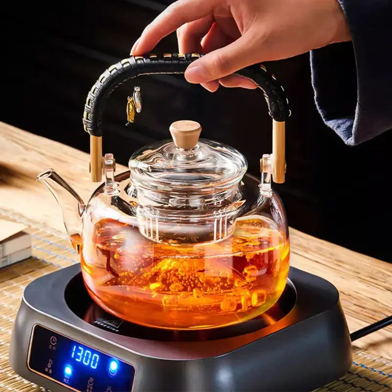 Clear glass decorbites glass tea pot with black weave handle wooden accents filled with amber tea