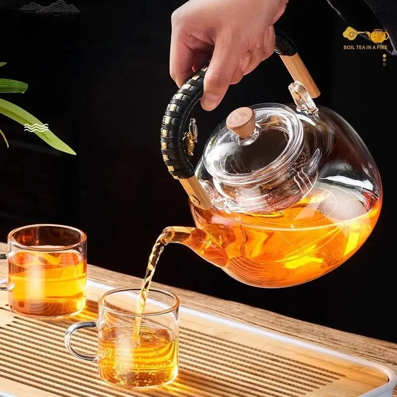 Clear glass DecorBites glass tea pot with wooden handle pouring amber tea into matching glass cups with wooden lid knob