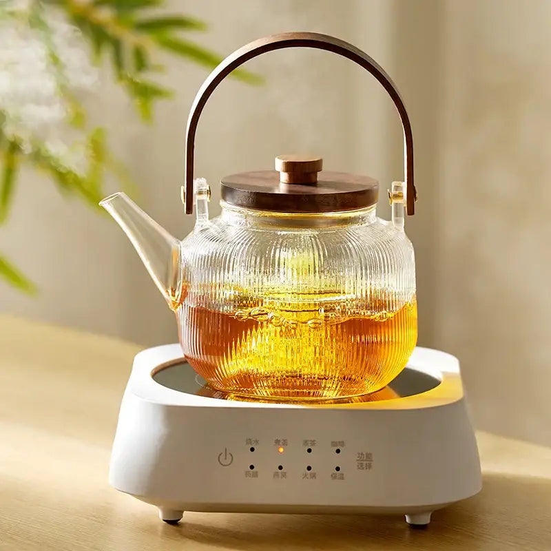 Clear ribbed glass tea pot with wooden handle and lid on a white electric heating base by DecorBites glass tea pot