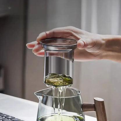 Decorbites™ glass tea set with solid wood handle and metal rim straining green leaves into clear glass teapot