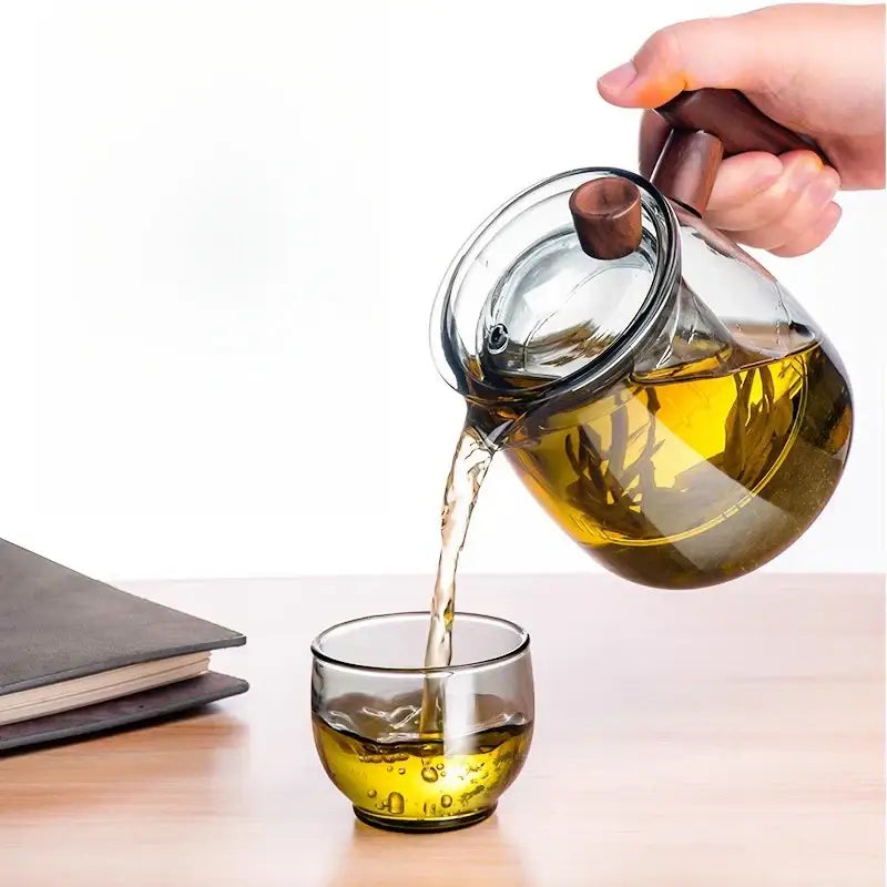 Clear glass DecorBites glass tea set with solid wood handle pouring golden tea into matching glass cup with tea separation technology