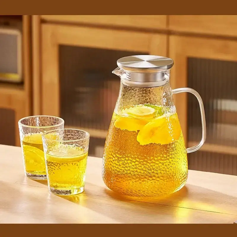 Clear hammered glass tea set pitcher with stainless steel silver lid and handle filled with lemon-infused liquid from decorbites
