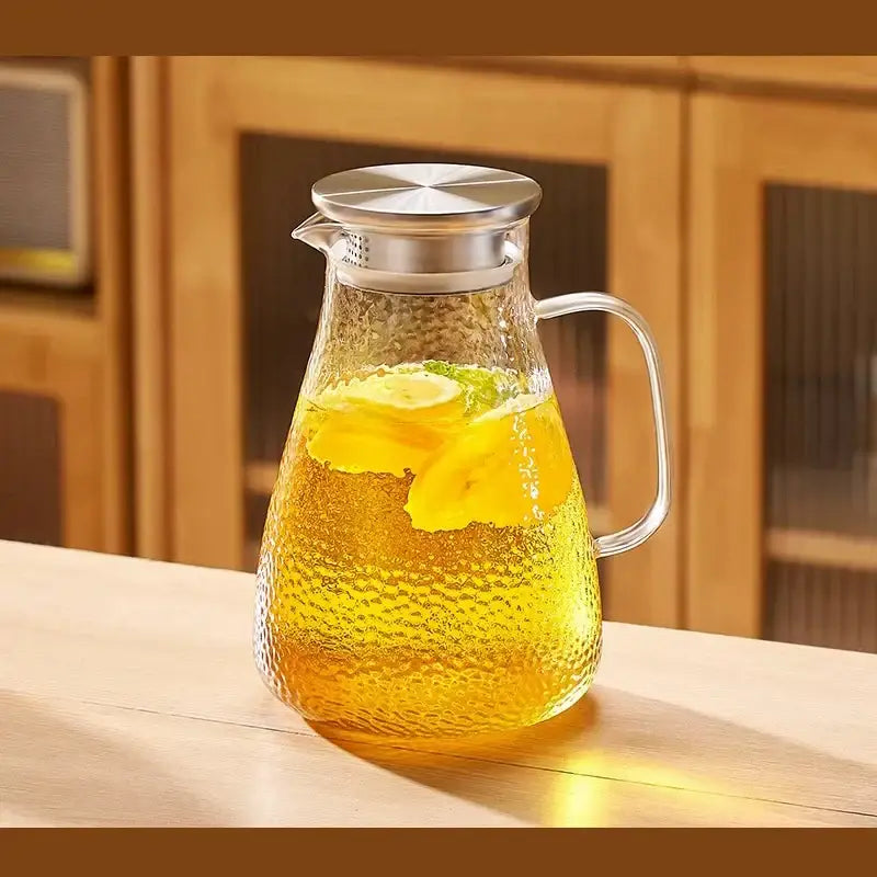 Clear textured glass pitcher with silver stainless steel lid and handle filled with lemon tea in decorbites glass tea set
