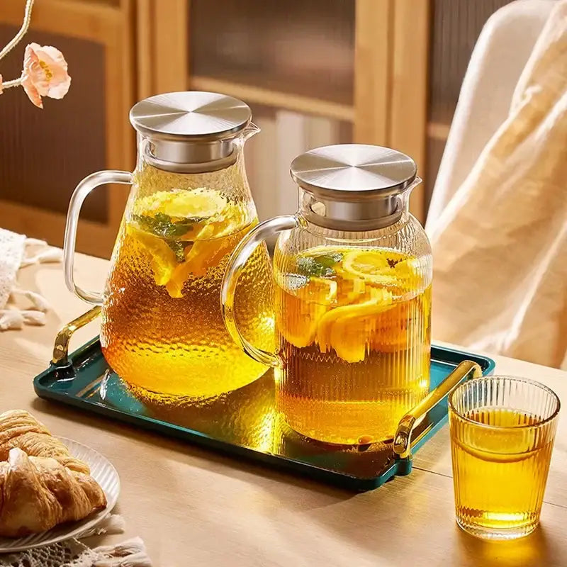 Two clear glass pitchers with textured surfaces and silver lids filled with citrus tea from decorbites glass tea set