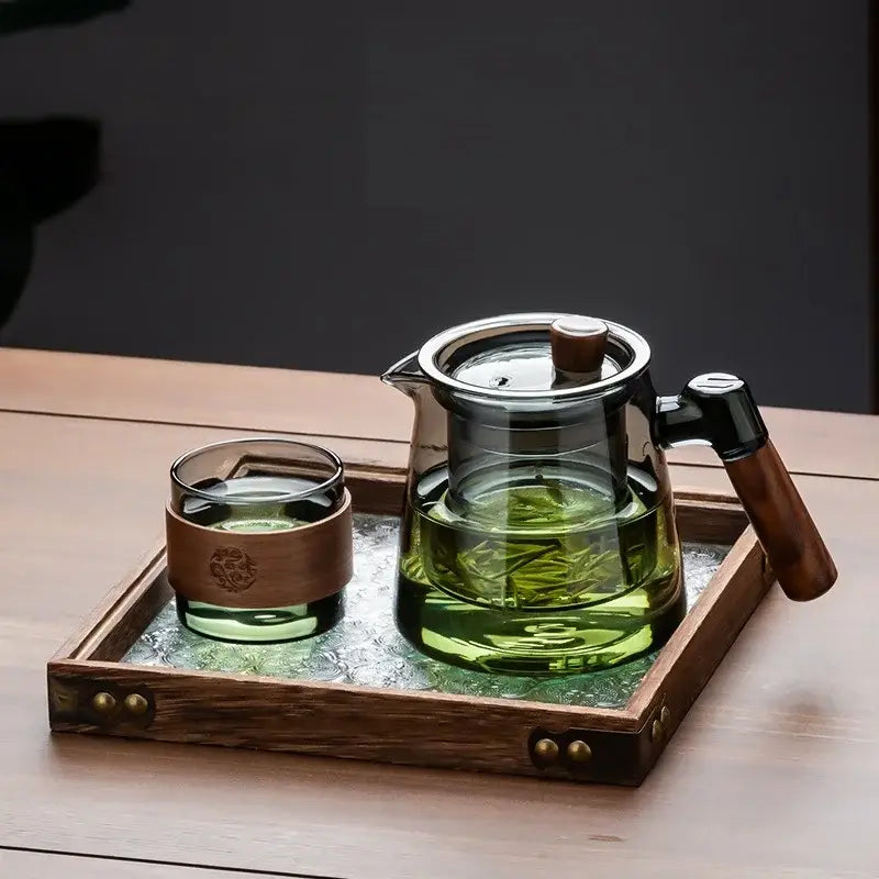 Clear glass teapot with wooden handle and lid filled with green tea on retro glass tray in DecorBites tea set