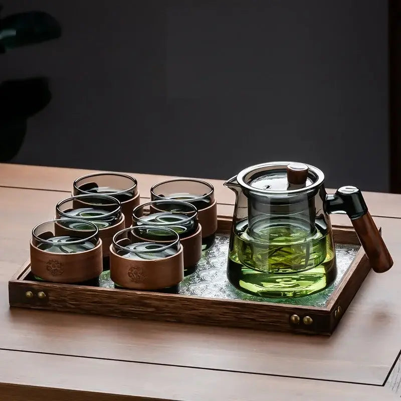 Clear glass teapot with wooden handle and lid knob filled with green tea on retro glass tray from decorbites tea set