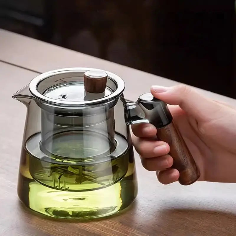 A clear glass teapot with a wooden handle and stainless steel strainer on a retro glass tray from decorbites tea set