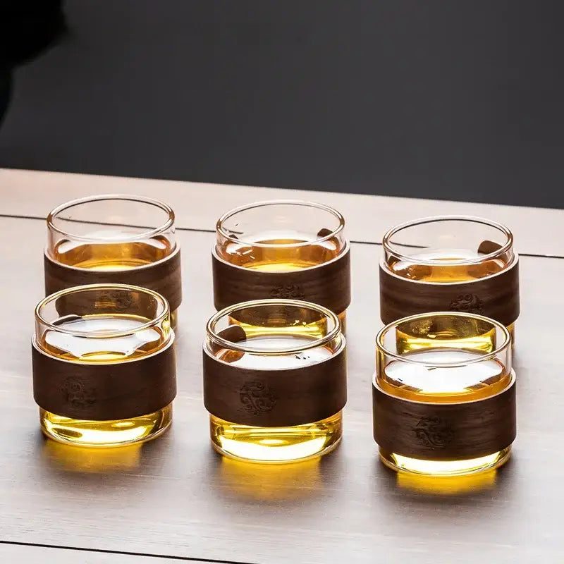 Set of six clear glass tea cups with wooden bands filled with amber tea on a retro glass tray from DecorBites tea set