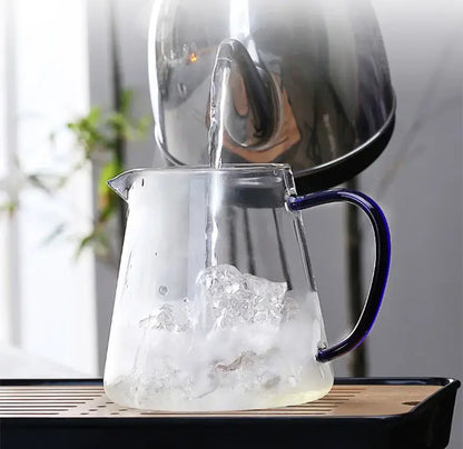 A decorbites glass teapot 550ml with a blue handle is being filled with hot water from a stainless steel kettle