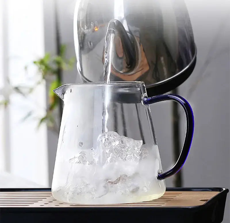 A clear glass teapot with a sleek blue handle is being filled with hot water from a stainless steel kettle decorbites glass teapot