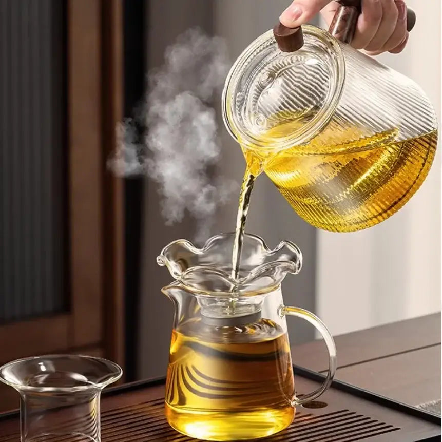 A clear decorbites glass teapot 900ML with ribbed design and wooden handle pouring golden tea into matching glass pitcher