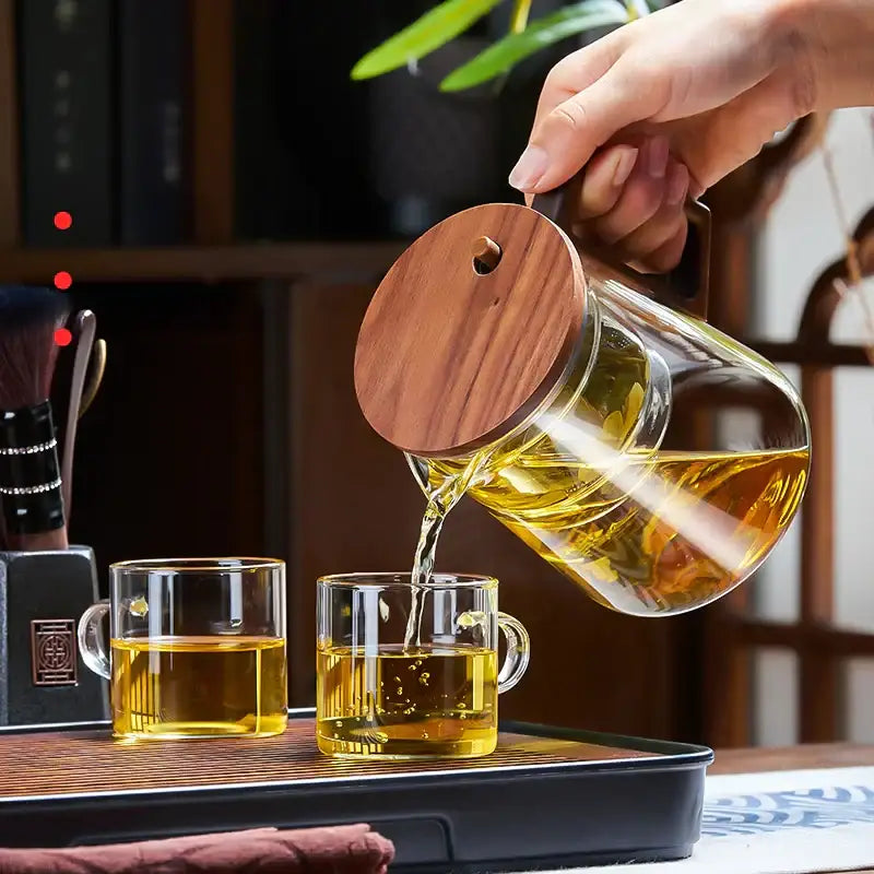 Decorbites glass teapot filter kettle set in clear glass with wooden lid pouring golden tea into matching cups