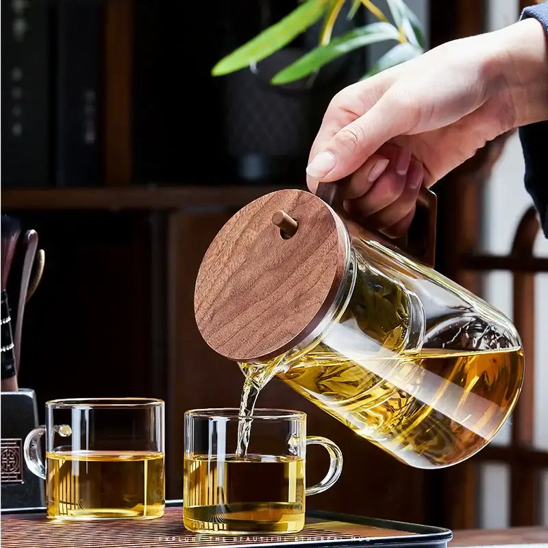 Decorbites glass teapot filter kettle with warm brown wooden lid and handle pouring golden tea into clear cups