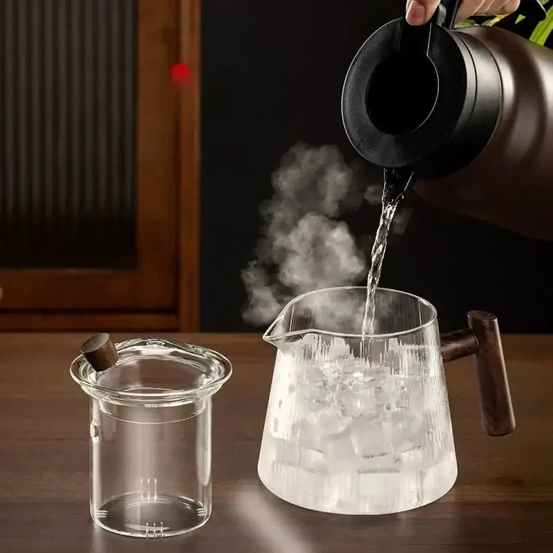 A decorbites glass teapot with transparent high borosilicate body and wooden handle being filled from a black kettle