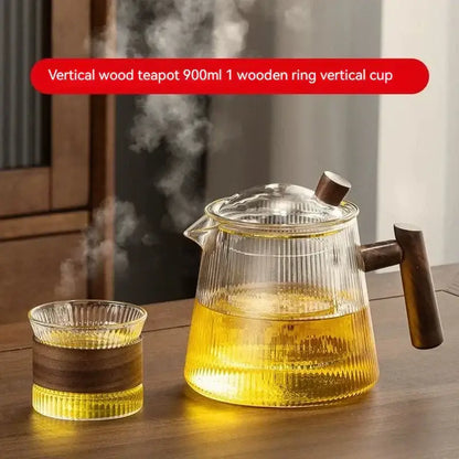 Vertical decorbites glass teapot with dark wood handle and lid filled with steaming golden tea made of high borosilicate