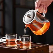 Clear glass decorbites glass teapot with silver lid pouring amber tea into matching cups for puer tea and coffee