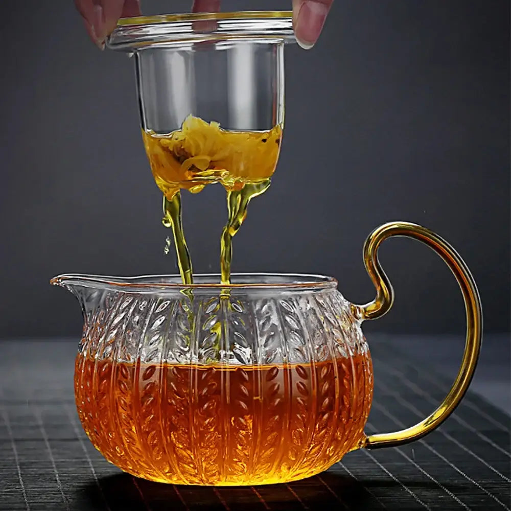 Clear glass teapot with gold handle and leaf embossing filled with amber tea from decorbites glass teapot collection
