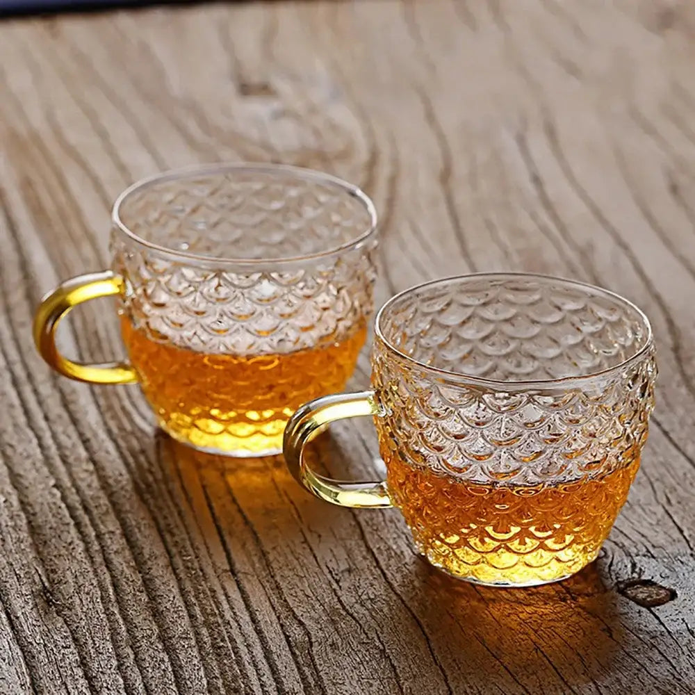 Clear glass mugs with scalloped texture and golden handles filled with amber liquid from decorbites glass teapot set