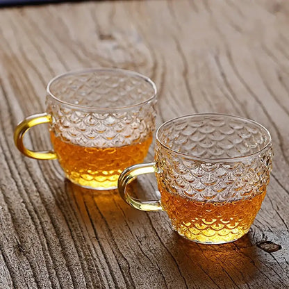 Clear glass mugs with scalloped texture and golden handles filled with amber liquid from decorbites glass teapot set