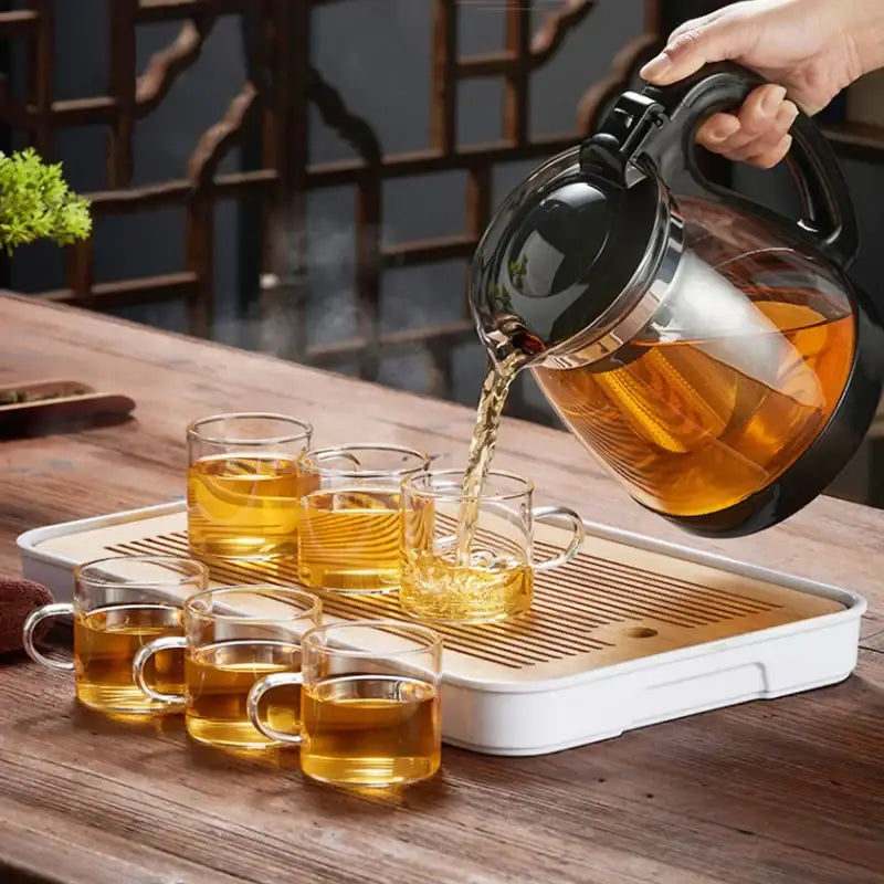 Black-handled decorbites glass teapot with silver rim pouring amber tea into clear glass cups from large capacity filter set