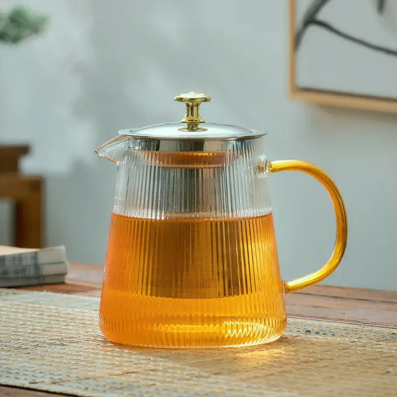 DecorBites glass teapot with vertical ridges and golden handle filled with amber tea for office home use
