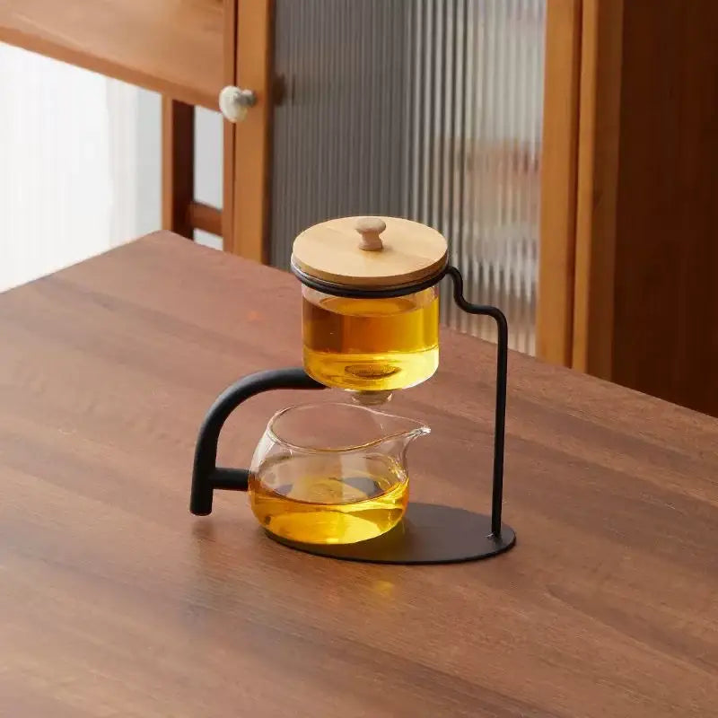 Decorbites glass teapot set with clear glass infuser, bamboo lid, and black metal stand filled with golden amber tea