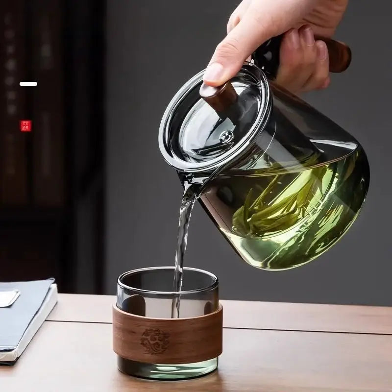 Clear glass decorbites glass teapot set with wooden handle pouring green tea into glass cup with bamboo sleeve
