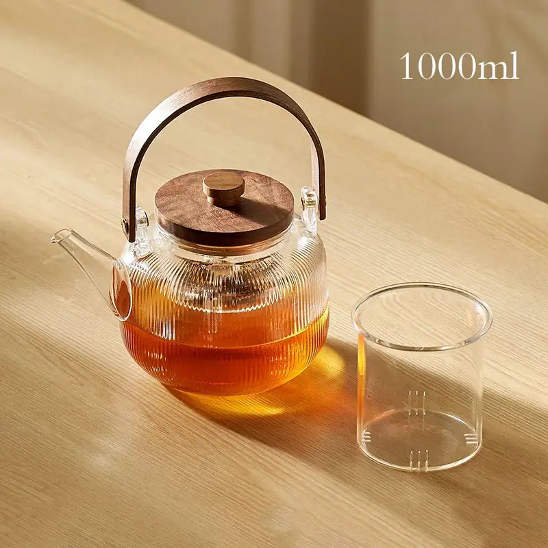A 1000ml decorbites glass teapot set with wooden handle and cover filled with amber tea in clear glass