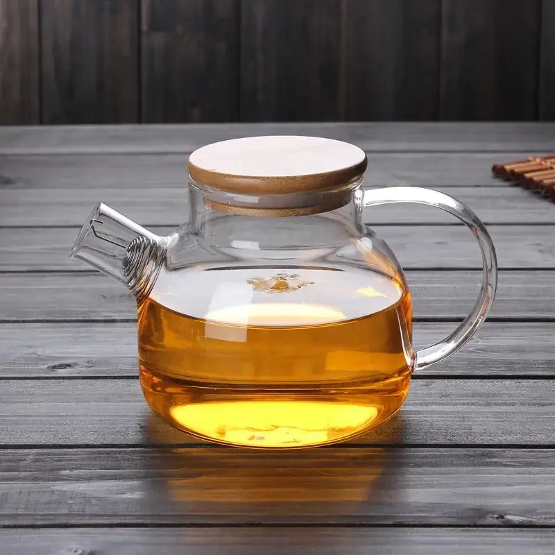 Clear glass decorbites glass teapot with wooden lid and curved handle filled with amber tea for tea brewing