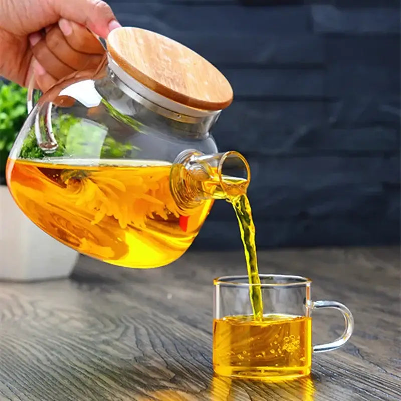 Clear glass decorbites glass teapot with wooden lid pouring golden tea into a matching mug for tea brewing