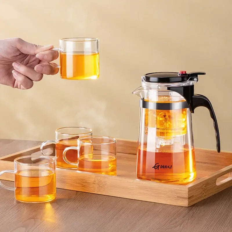 Clear glass decorbites glass teapot with black lid handle and one-button filter holding golden tea on wooden tray