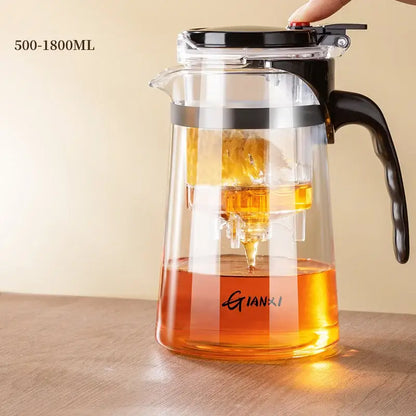 Clear glass honey dispenser with black lid and handle featuring a built-in strainer for easy pouring by decorbites glass teapot
