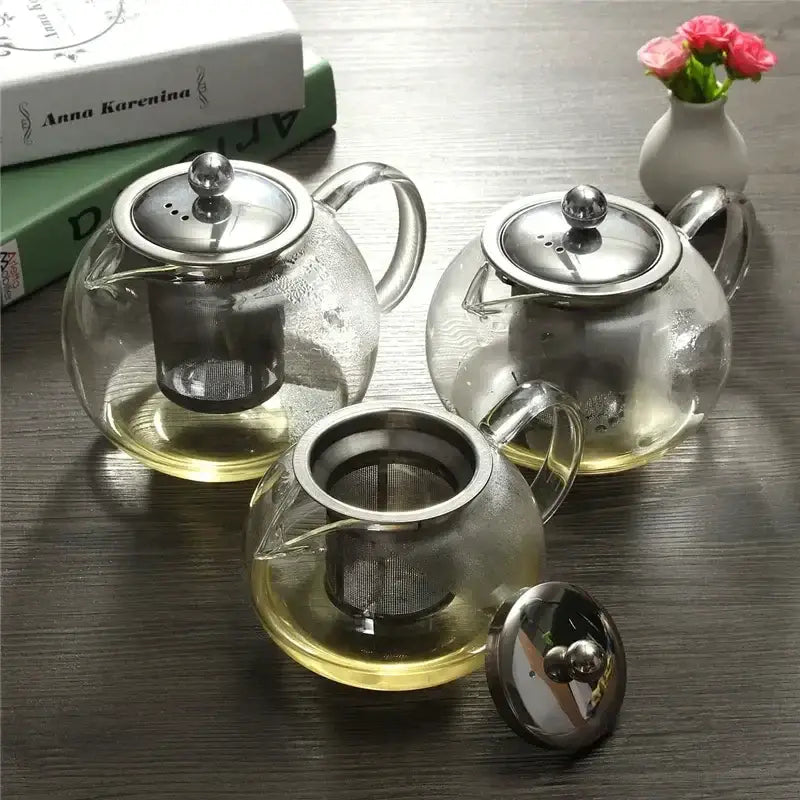 Three clear borosilicate glass teapots with stainless steel infuser lids filled with golden flower tea by decorbites