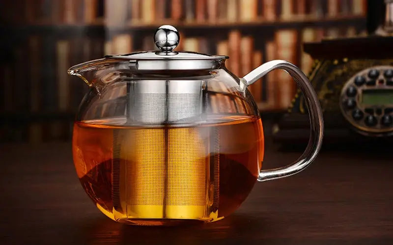 Clear borosilicate glass teapot with stainless steel infuser and amber flower tea inside by decorbites