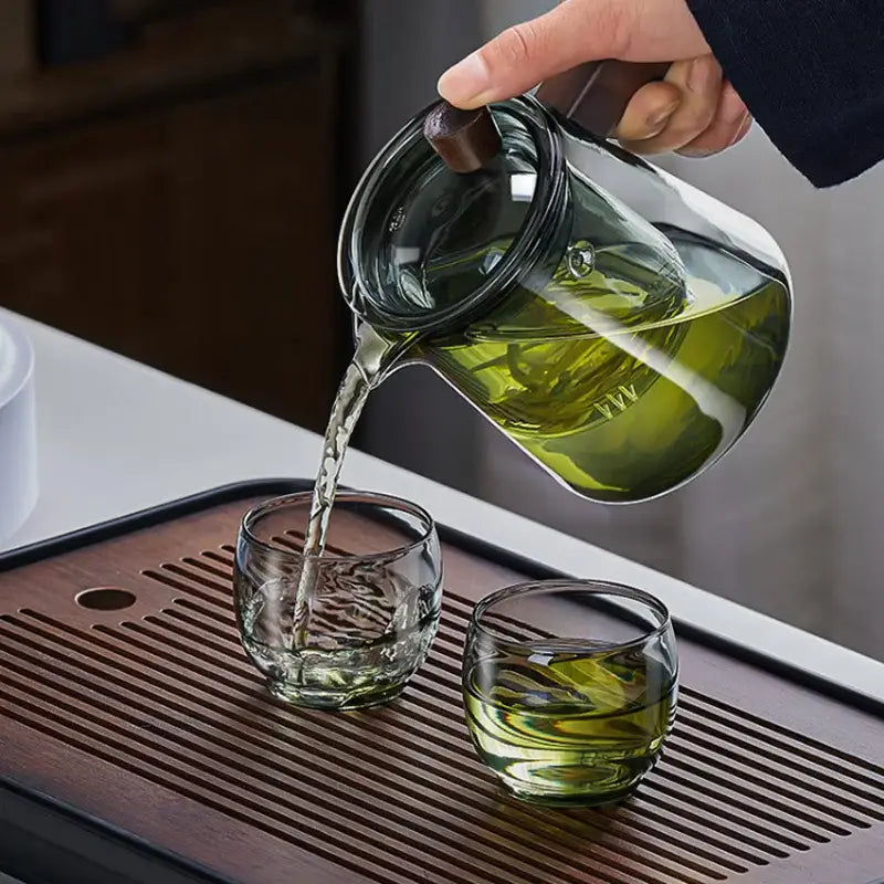 Clear glass teapot with dark wood handle pouring green tea into textured glass cups decorbites glass teapot set
