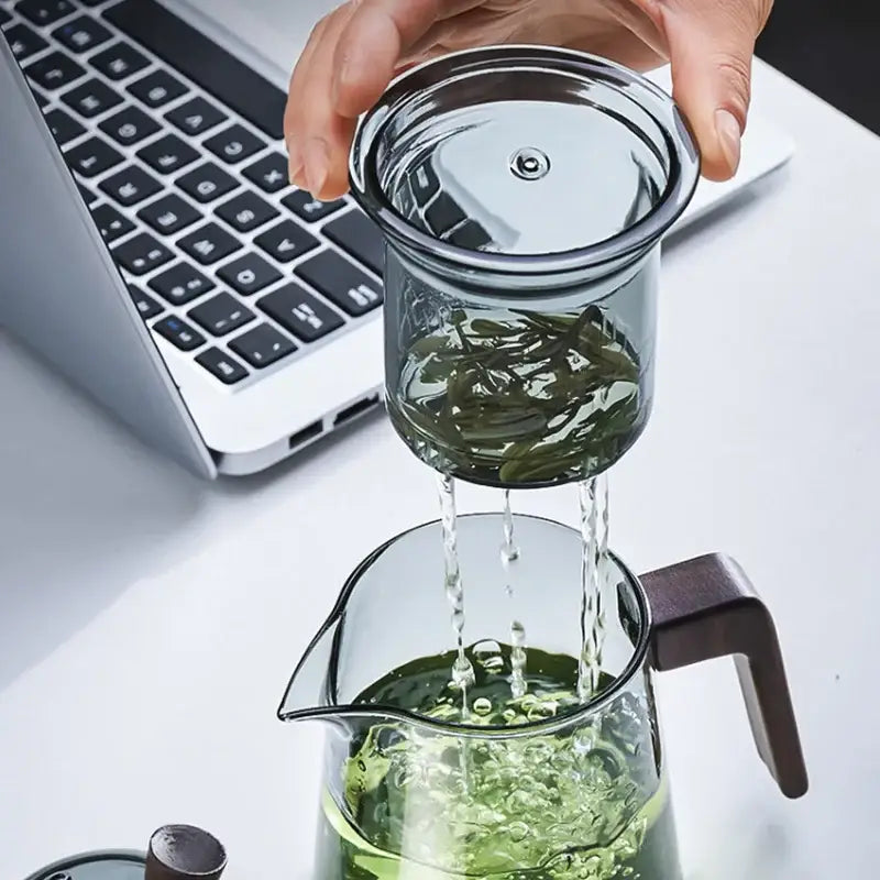 Clear glass teapot with dark brown wood handle pouring hot water through green tea leaves by decorbites glass teapot