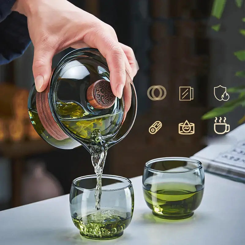 Clear glass decorbites glass tureen teapot with wooden lid pouring green tea into matching cups for kung fu tea set