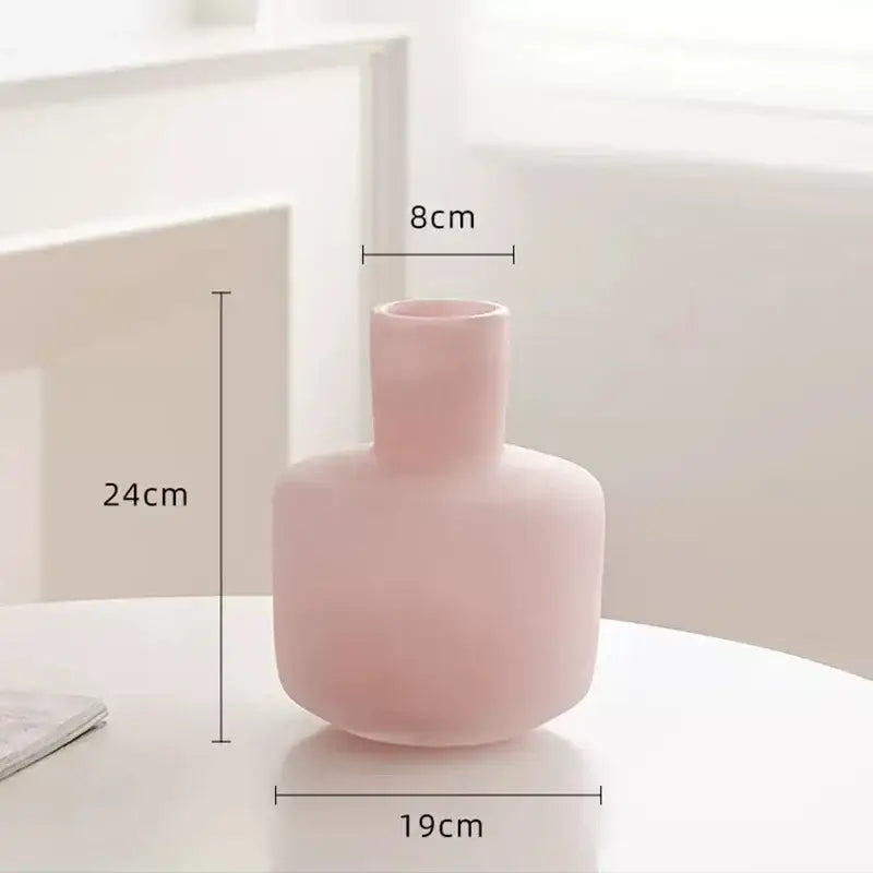 A soft pink ceramic decorbites glass vase with a rounded body and narrow neck for artificial flowers on a glass vase desk