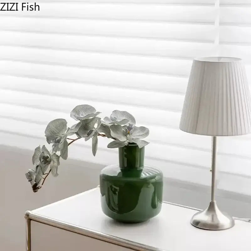 A decorbites glass vase desk decoration pot in glossy emerald green ceramic holding silver-toned artificial flowers