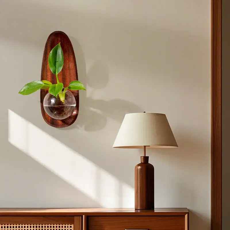 A sleek oval wooden wall-mounted decorbites glass vase flowerpot with a clear sphere holding vibrant green leaves