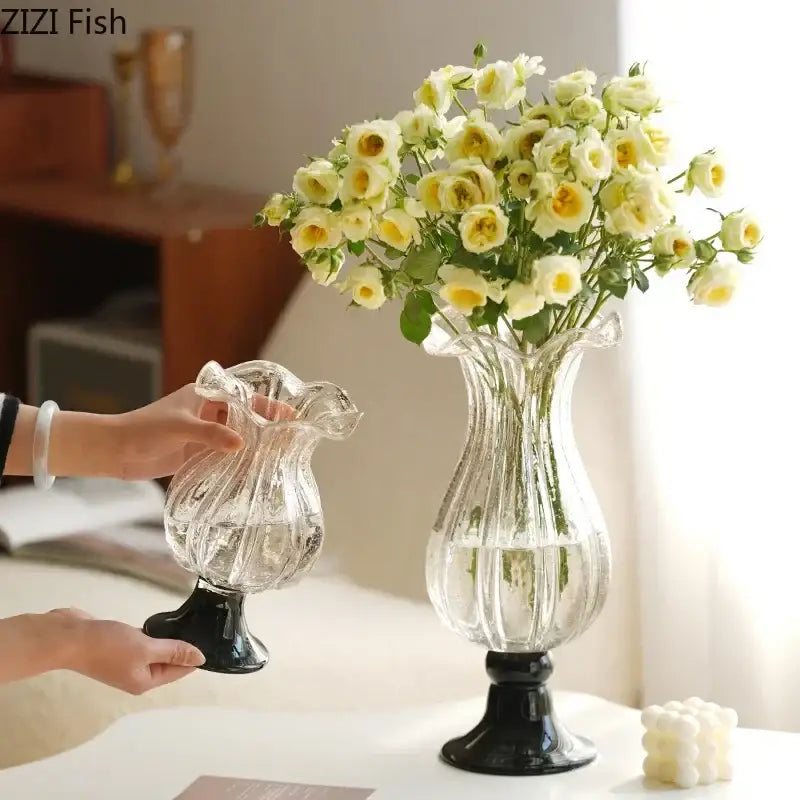 Clear glass vase with black pedestal base and ribbed texture holding pale yellow roses by DecorBites glass vase