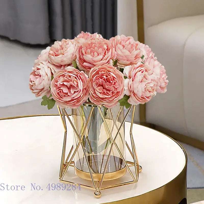 A bouquet of soft pink peonies arranged in a modern decorbites glass vase with gold metal frame and clear glass vase metal design
