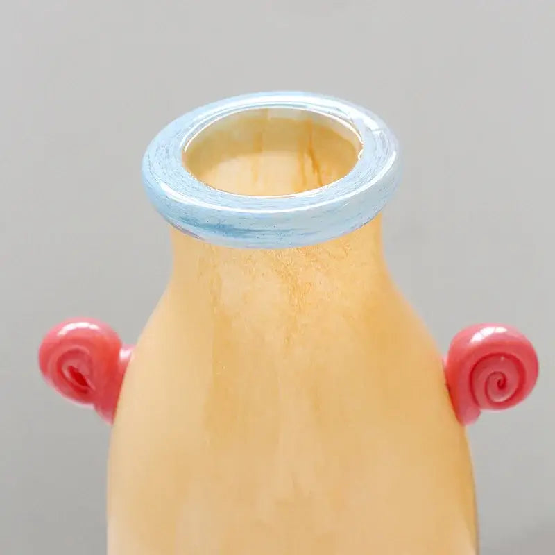 A peach-colored DecorBites glass vase with light blue rim and pink spiral candy handles for home decor and floral arrangements