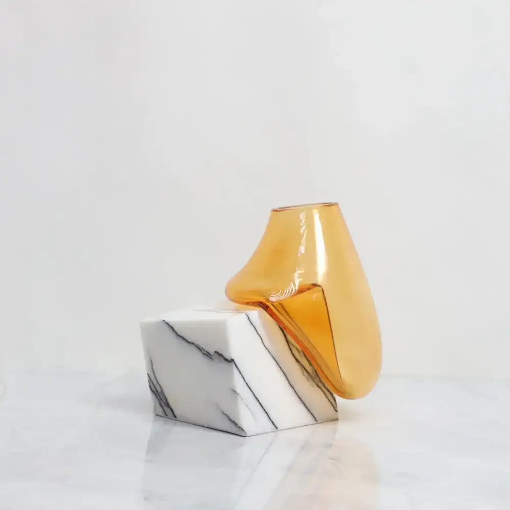 A decorbites glass vase in translucent amber with smooth curves on a white marble base for elegant home décor